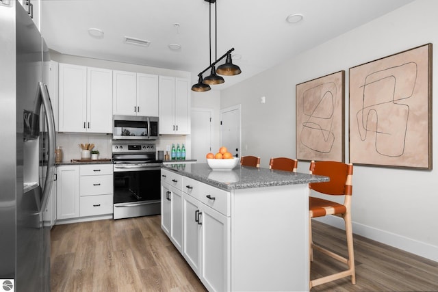 kitchen featuring hanging light fixtures, a breakfast bar, white cabinets, stainless steel appliances, and a center island