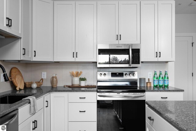 kitchen with dark stone countertops, white cabinets, appliances with stainless steel finishes, and sink