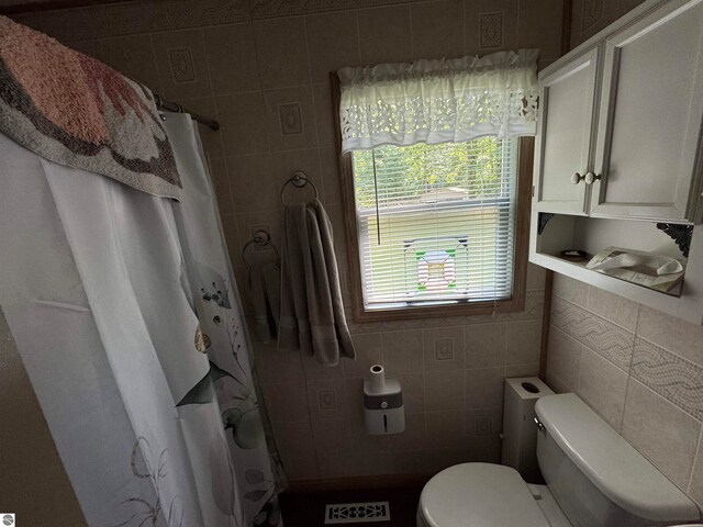 bathroom with walk in shower, tile walls, and toilet