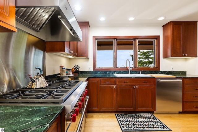 kitchen with dark stone counters, light hardwood / wood-style floors, sink, exhaust hood, and appliances with stainless steel finishes