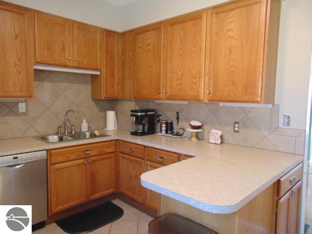 kitchen with light tile patterned flooring, sink, kitchen peninsula, dishwasher, and decorative backsplash