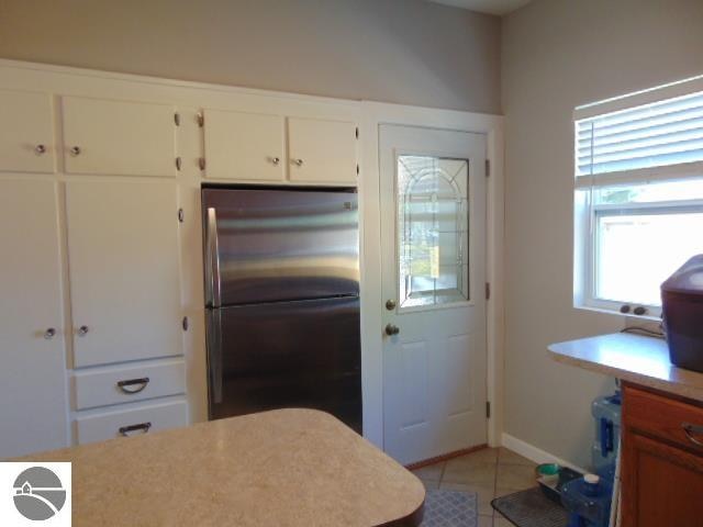 kitchen with white cabinets, light tile patterned flooring, and stainless steel refrigerator