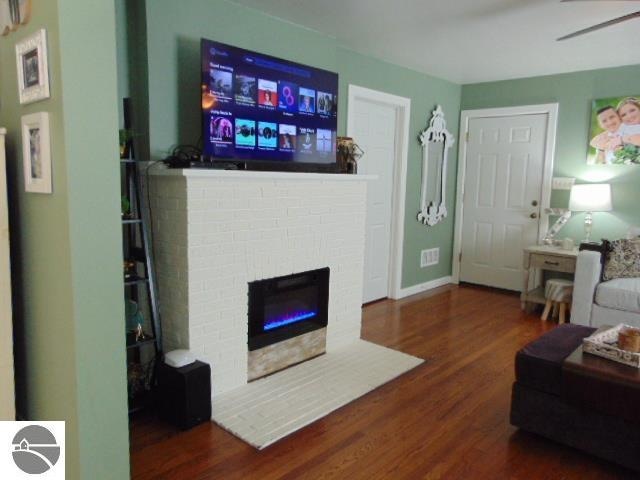 living room with a brick fireplace, ceiling fan, and dark wood-type flooring