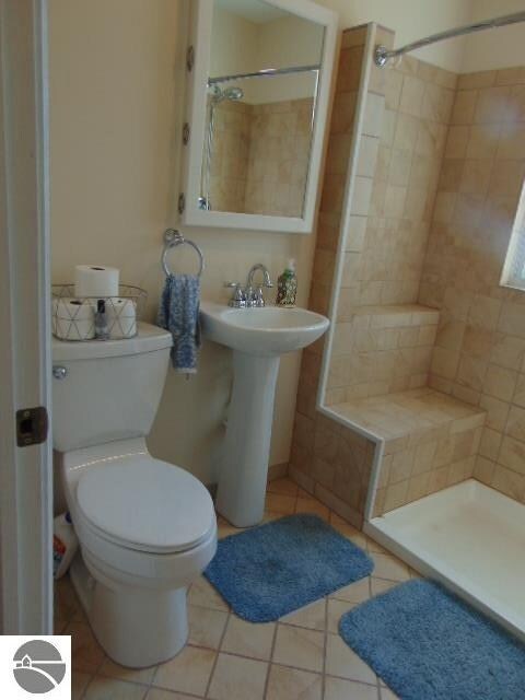 bathroom with a tile shower, toilet, and tile patterned floors