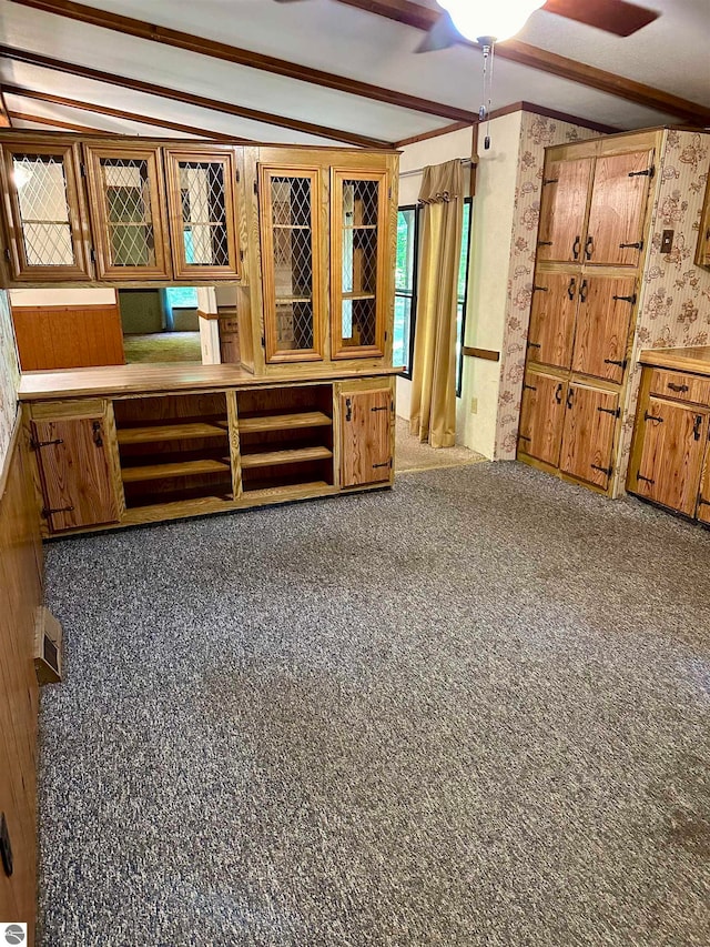 unfurnished living room featuring dark carpet, wood walls, ceiling fan, and lofted ceiling with beams