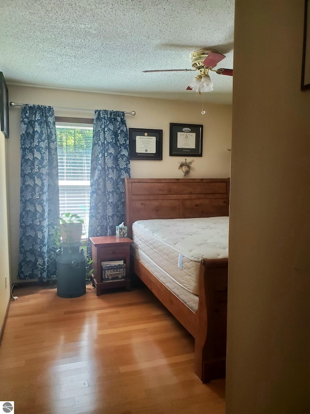 bedroom featuring ceiling fan, wood-type flooring, and a textured ceiling