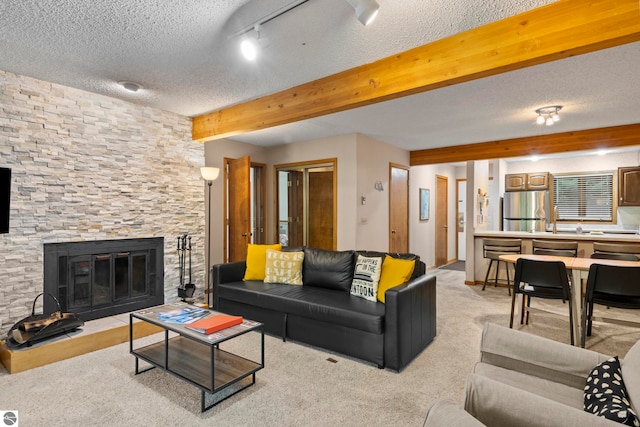 carpeted living room featuring a textured ceiling, beamed ceiling, and a stone fireplace