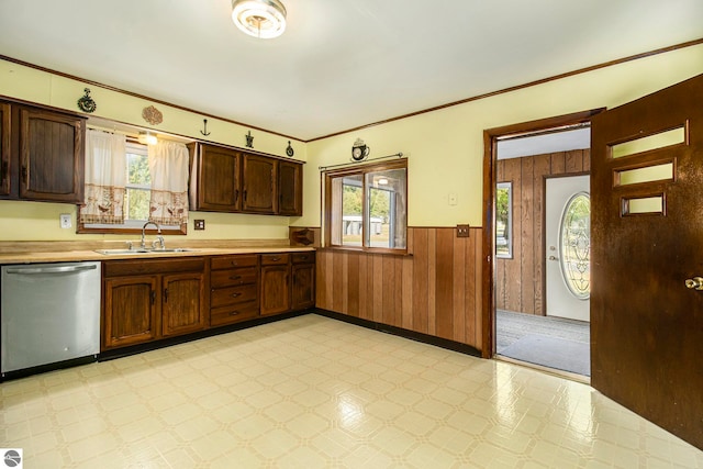 kitchen featuring dark brown cabinets, stainless steel dishwasher, wooden walls, and sink