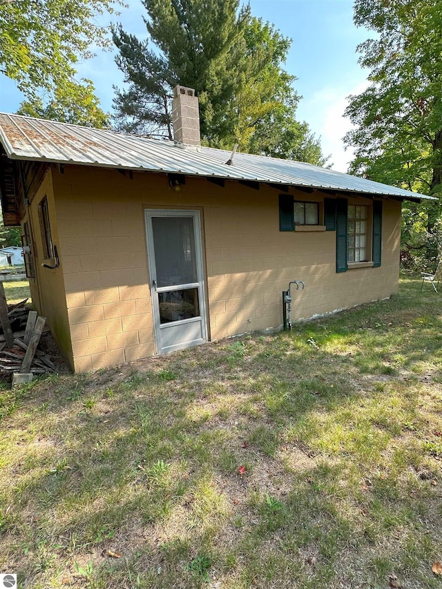 rear view of property with a chimney, concrete block siding, a yard, and metal roof