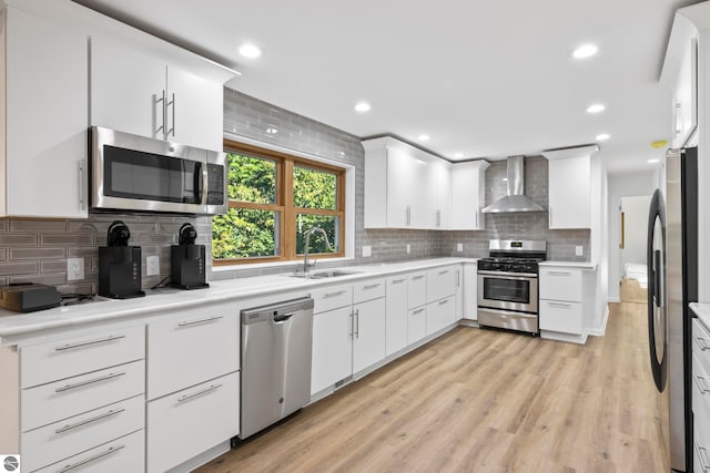 kitchen featuring sink, wall chimney exhaust hood, light hardwood / wood-style flooring, stainless steel appliances, and decorative backsplash