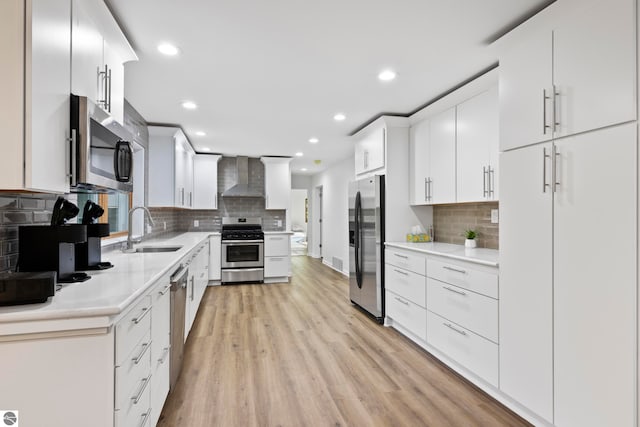 kitchen with white cabinets, stainless steel appliances, light hardwood / wood-style flooring, sink, and wall chimney range hood