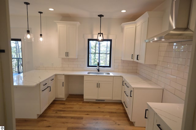 kitchen featuring white cabinetry, sink, wall chimney exhaust hood, hanging light fixtures, and light stone counters