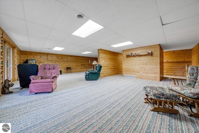 sitting room featuring a drop ceiling, wood walls, and carpet flooring