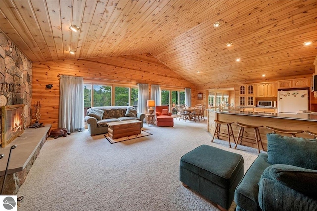 carpeted living room with wood walls, wood ceiling, high vaulted ceiling, and a stone fireplace