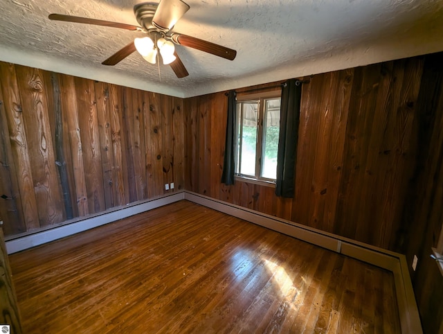 unfurnished room with wood-type flooring, ceiling fan, wooden walls, and a textured ceiling