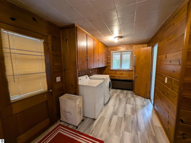 clothes washing area featuring light hardwood / wood-style floors, cabinets, wooden walls, and independent washer and dryer