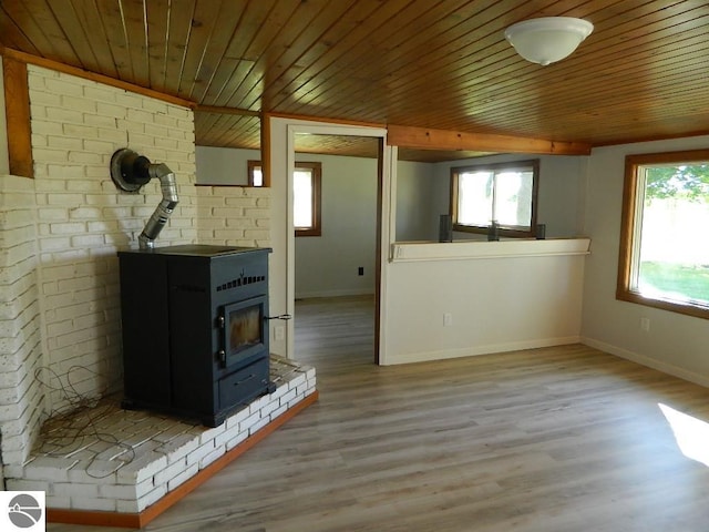 unfurnished living room featuring brick wall, light hardwood / wood-style floors, a wood stove, and wooden ceiling