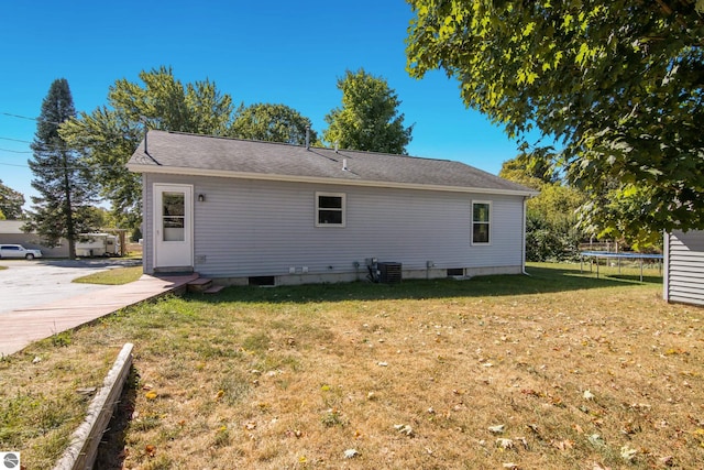 rear view of property with a trampoline, a yard, and central AC