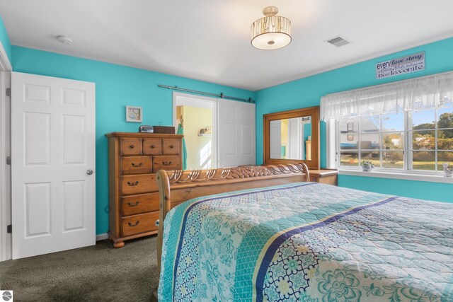 bedroom with a barn door and dark carpet