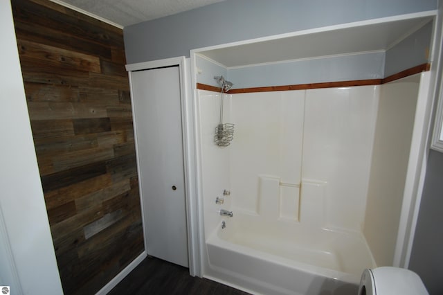 bathroom featuring a textured ceiling, wood walls, toilet, and shower / bath combination