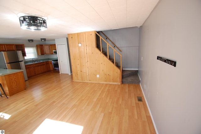 unfurnished living room featuring light wood-type flooring, wood walls, and sink