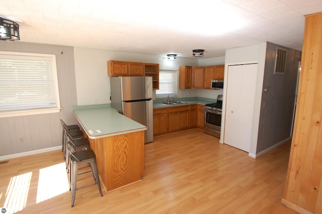 kitchen featuring appliances with stainless steel finishes, light hardwood / wood-style floors, kitchen peninsula, a kitchen bar, and sink