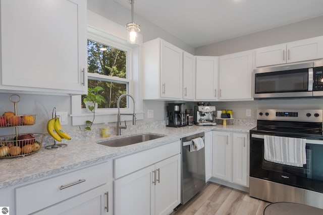 kitchen with pendant lighting, sink, white cabinetry, stainless steel appliances, and light hardwood / wood-style floors