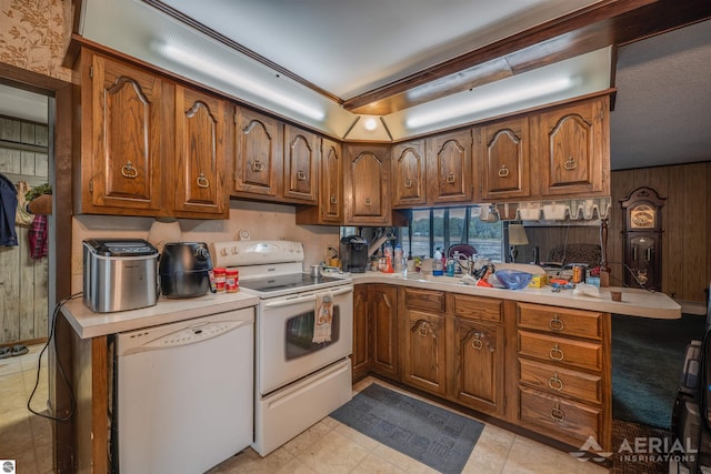 kitchen with light tile patterned flooring, kitchen peninsula, white appliances, and wood walls