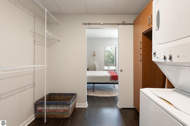 laundry room with stacked washer / drying machine, dark wood-type flooring, and a barn door