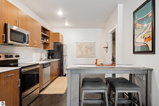 kitchen with appliances with stainless steel finishes, a kitchen bar, sink, and dark wood-type flooring