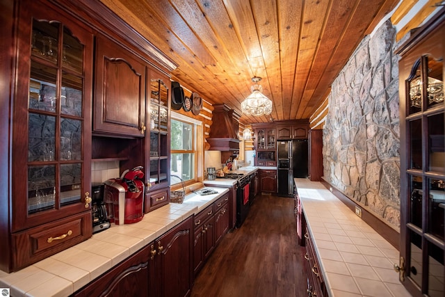 kitchen featuring tile counters, hardwood / wood-style flooring, custom exhaust hood, black appliances, and wooden ceiling