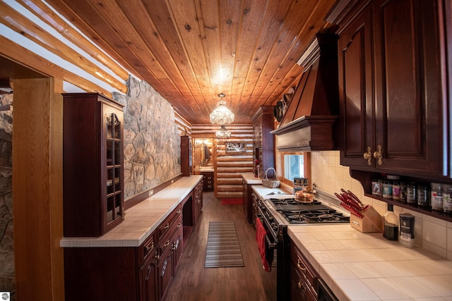 kitchen with tile counters, hardwood / wood-style flooring, stainless steel stove, custom range hood, and rustic walls