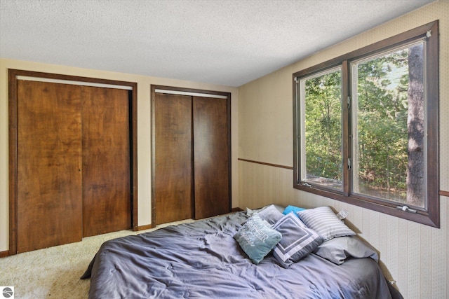 bedroom featuring two closets, a textured ceiling, and carpet flooring