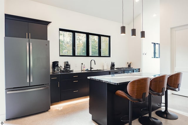 kitchen featuring hanging light fixtures, sink, stainless steel refrigerator, a breakfast bar, and light stone countertops