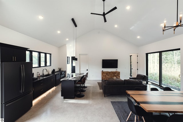 living room with ceiling fan with notable chandelier, a fireplace, sink, and high vaulted ceiling