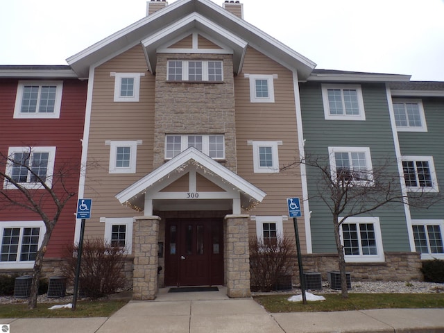 1246 Sunnyside Dr Unit 304Week 8, Cadillac, MI 49601 - view of front of house featuring stone siding, a chimney, and central AC unit