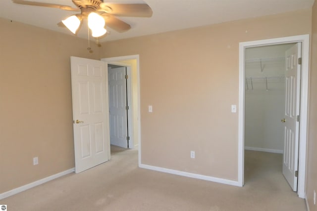 unfurnished bedroom with light carpet, a closet, ceiling fan, and a walk in closet