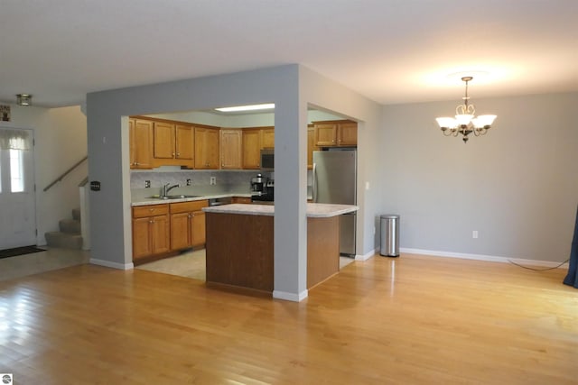 kitchen featuring hanging light fixtures, sink, backsplash, a notable chandelier, and light hardwood / wood-style floors