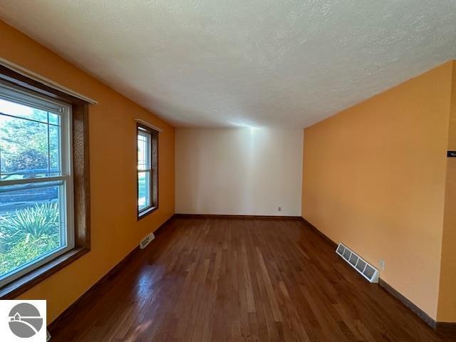 unfurnished room with a textured ceiling and dark wood-type flooring