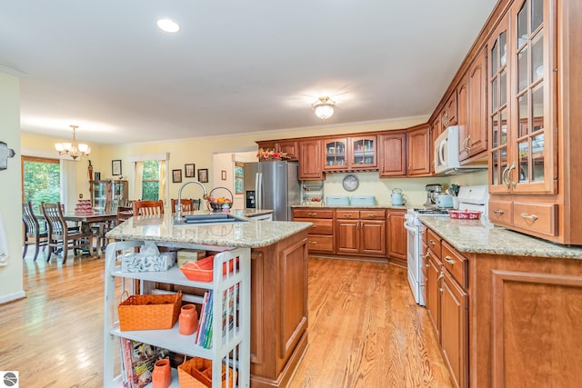 kitchen featuring hanging light fixtures, light hardwood / wood-style floors, an island with sink, white appliances, and sink