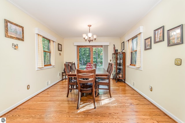 dining area with a notable chandelier, light wood-type flooring, and ornamental molding