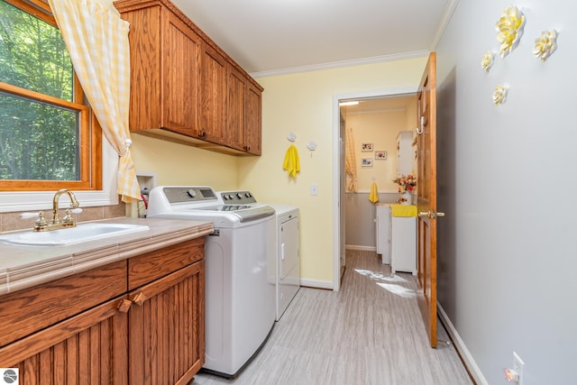 clothes washing area featuring sink, ornamental molding, cabinets, separate washer and dryer, and light wood-type flooring