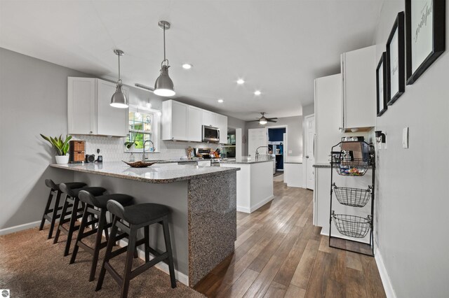 kitchen with white cabinetry, dark wood-type flooring, kitchen peninsula, stainless steel appliances, and decorative light fixtures