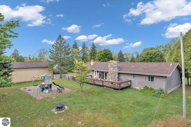 rear view of house featuring a wooden deck, a fire pit, a yard, and a playground