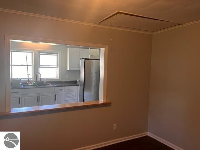 kitchen with stainless steel refrigerator, ornamental molding, sink, and white cabinets