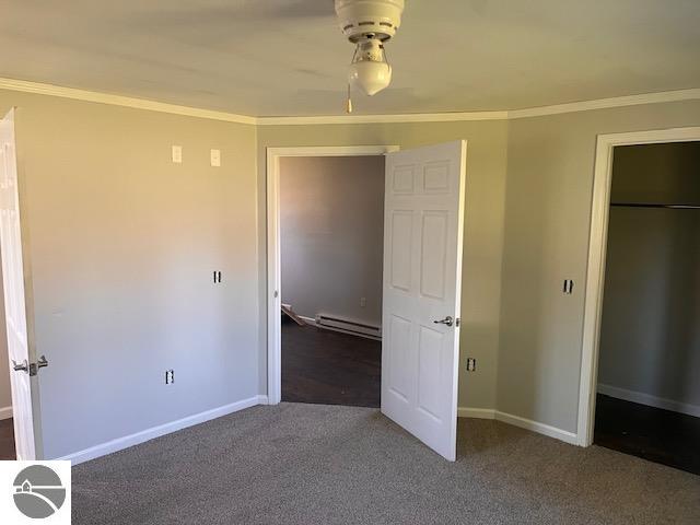 unfurnished bedroom with baseboard heating, a closet, crown molding, dark colored carpet, and ceiling fan