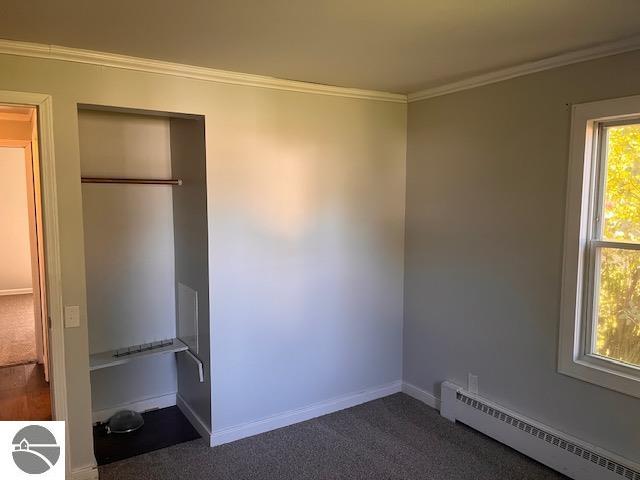 unfurnished bedroom with carpet floors, crown molding, and a baseboard heating unit