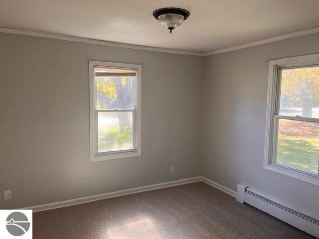 empty room featuring baseboard heating, ornamental molding, and dark carpet