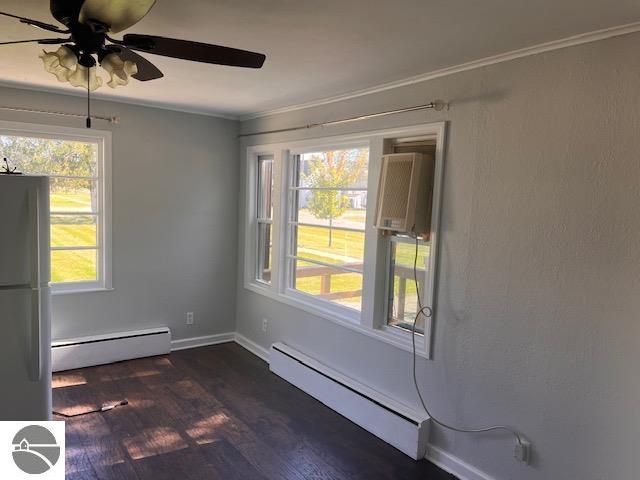 empty room with a wealth of natural light, dark wood-type flooring, and a baseboard radiator