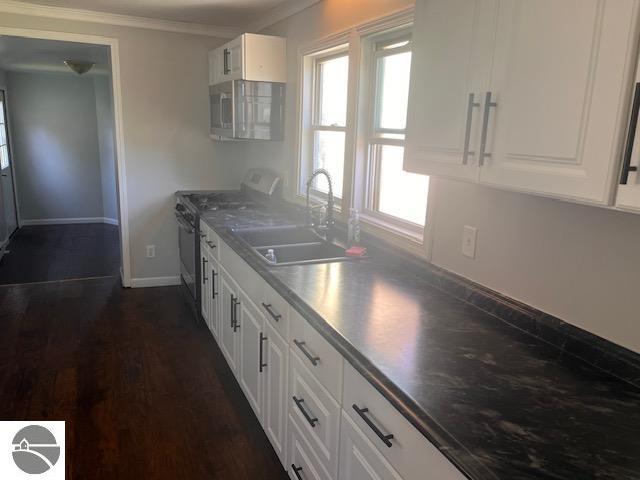 kitchen featuring dark hardwood / wood-style floors, sink, white cabinets, appliances with stainless steel finishes, and ornamental molding